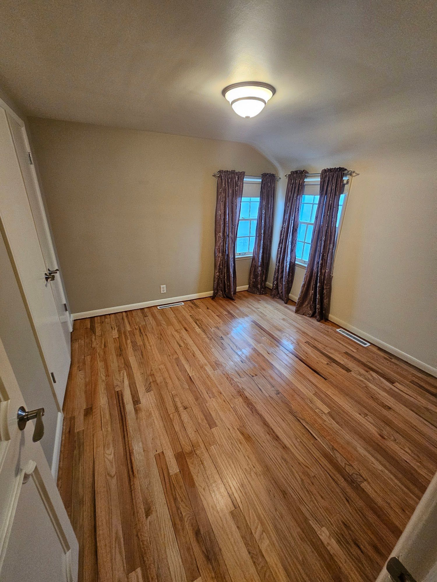 A large empty room with hardwood floors and two windows.