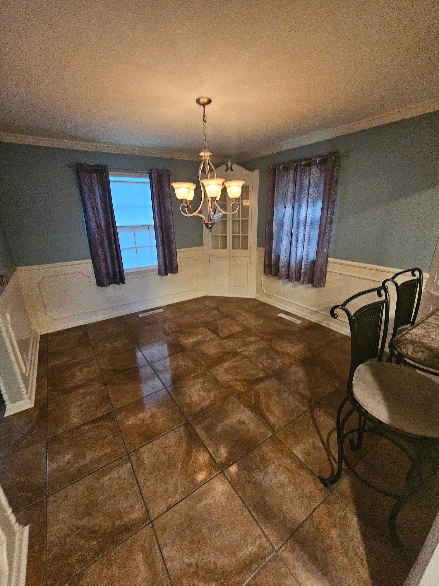 An empty dining room with a chandelier and a table and chairs.