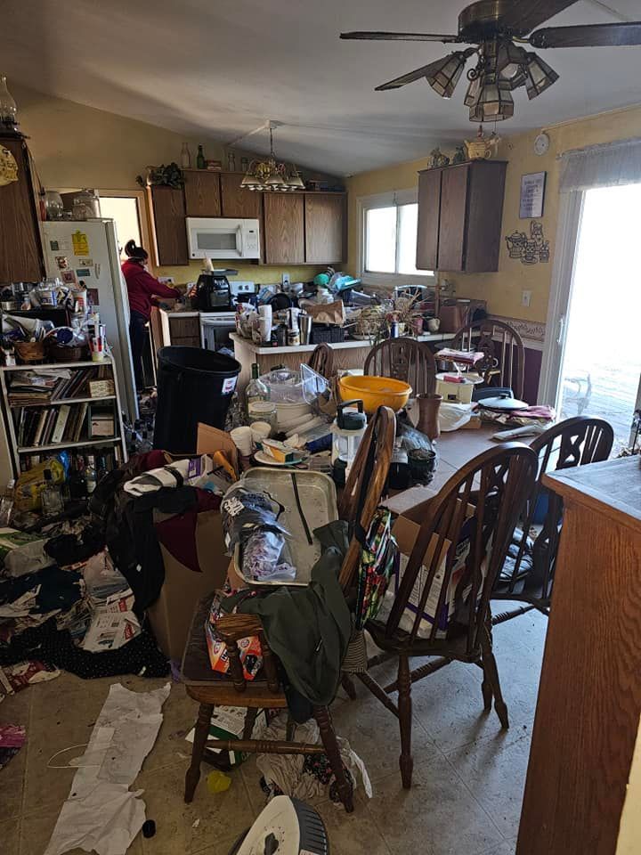 A kitchen and dining room in a messy house with a ceiling fan.
