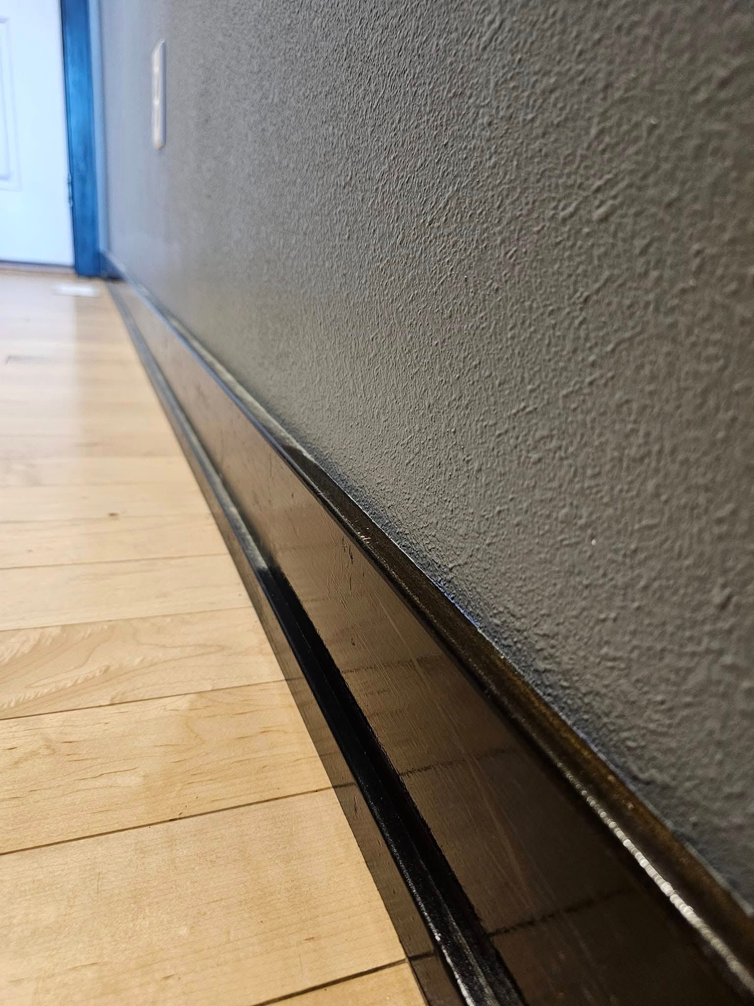 A hallway with a wooden floor and a gray wall.