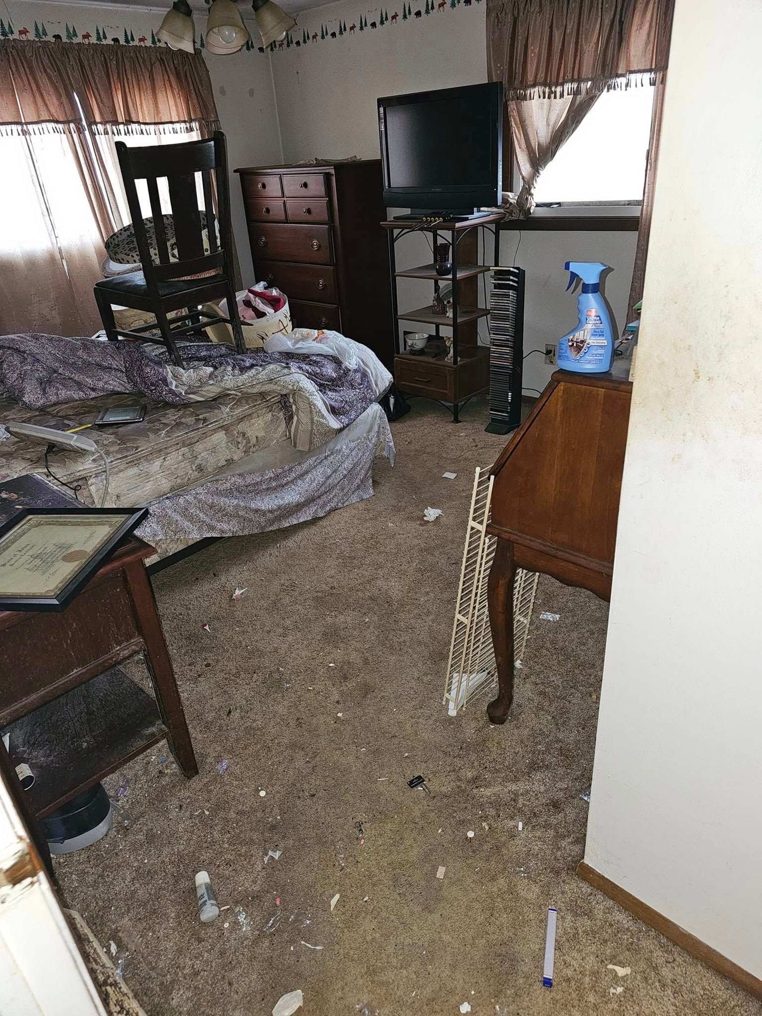 A bedroom with a messy carpet , a dresser , a desk and a television.