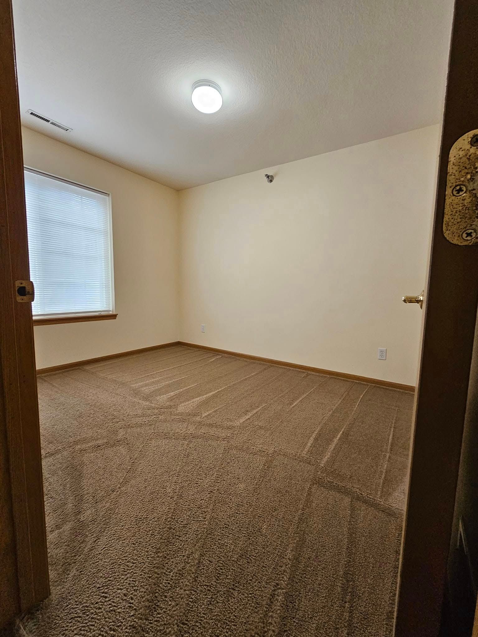 An empty bedroom with a carpeted floor and a window.