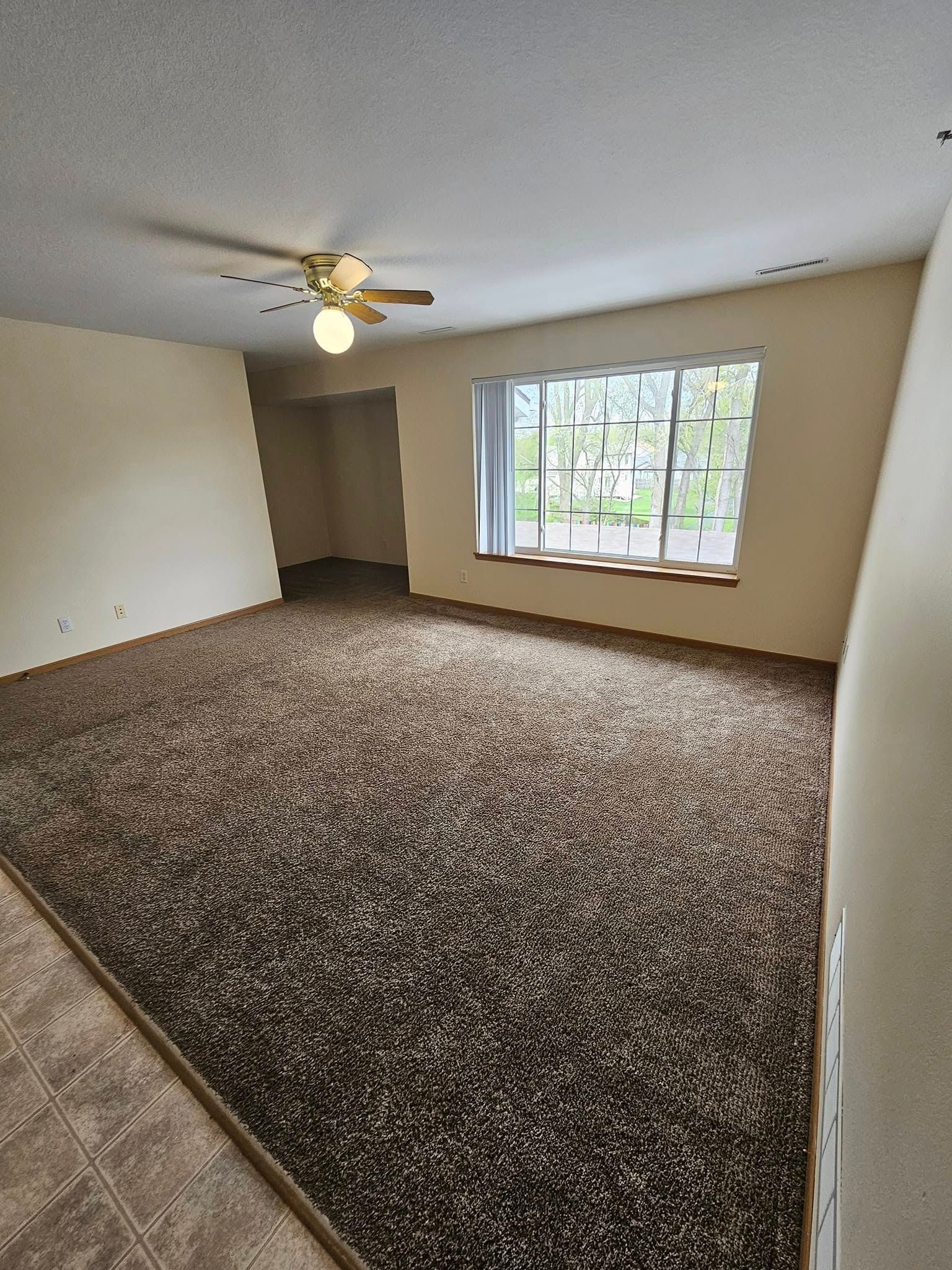 An empty living room with a ceiling fan and a window.