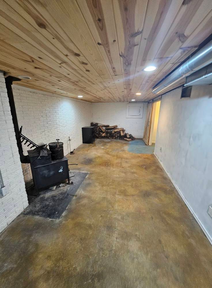 An empty basement with a wood stove and a wooden ceiling.