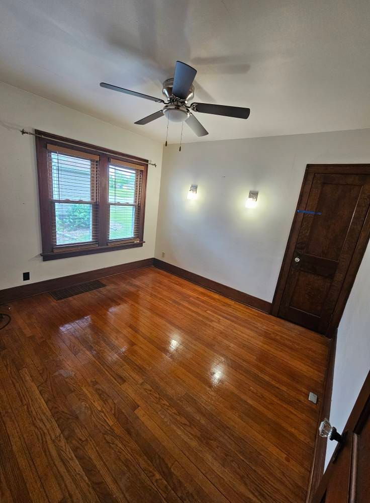 An empty room with hardwood floors and a ceiling fan.