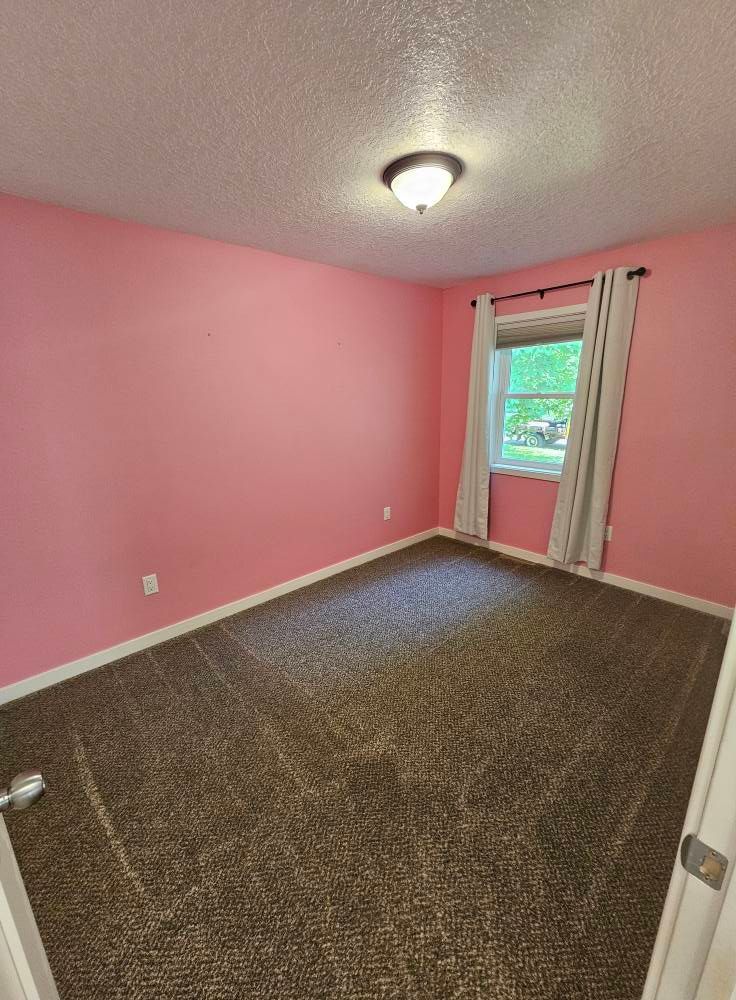 An empty bedroom with pink walls and a brown carpet.