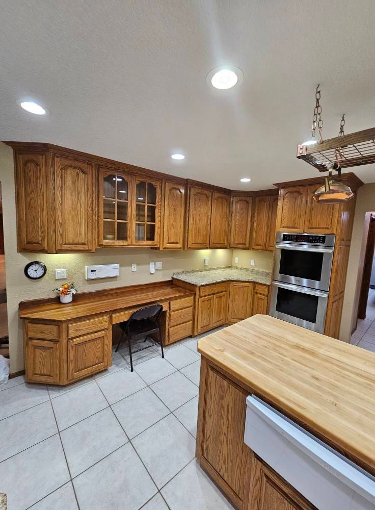 A kitchen with wooden cabinets , stainless steel appliances , a desk , and a large island.