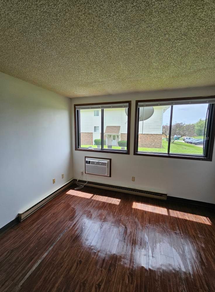 An empty living room with hardwood floors and two windows.