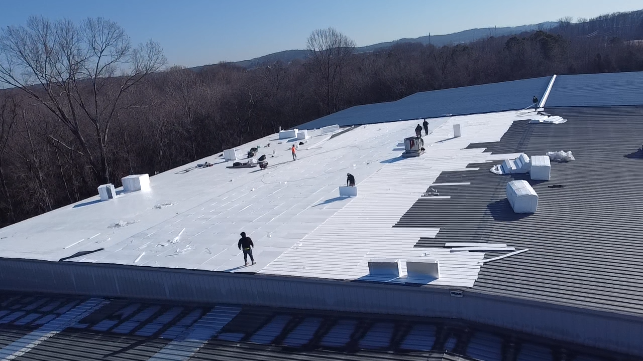 Workers install white roofing material on a building exterior under a clear blue sky.