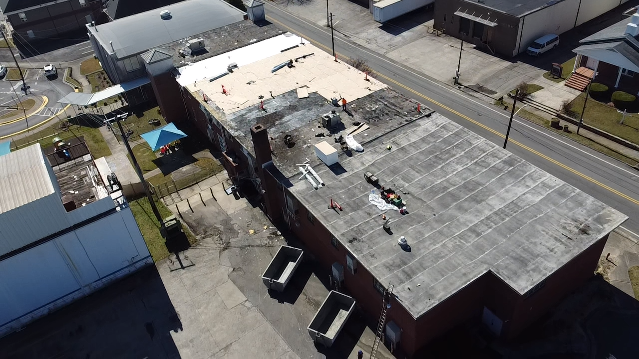 An aerial view of a rectangular building with a partially replaced tan roof alongside a darker, older roof section.