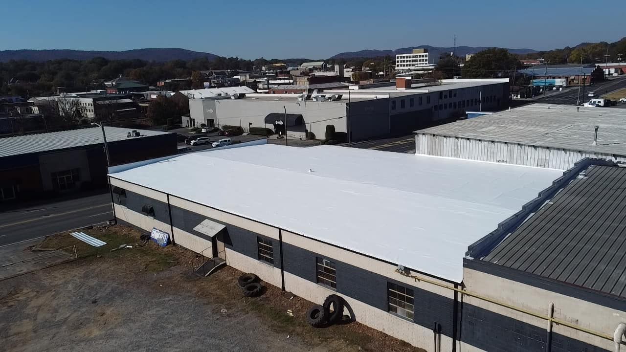 Aerial view of a commercial building with a newly installed white flat roof in a town setting.