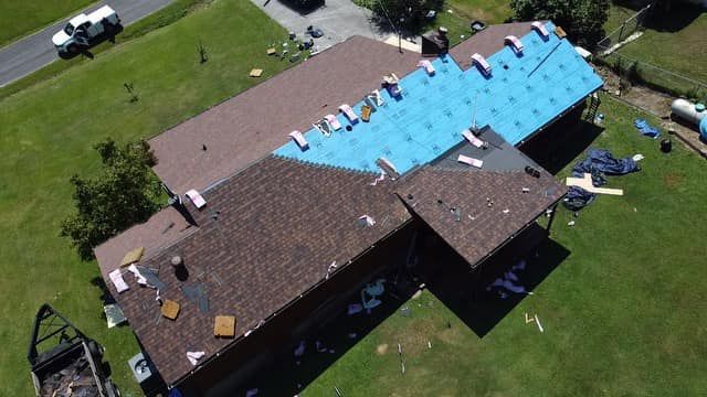 Aerial view of a residential roof undergoing repairs, showing sections with new brown shingles and blue underlayment.