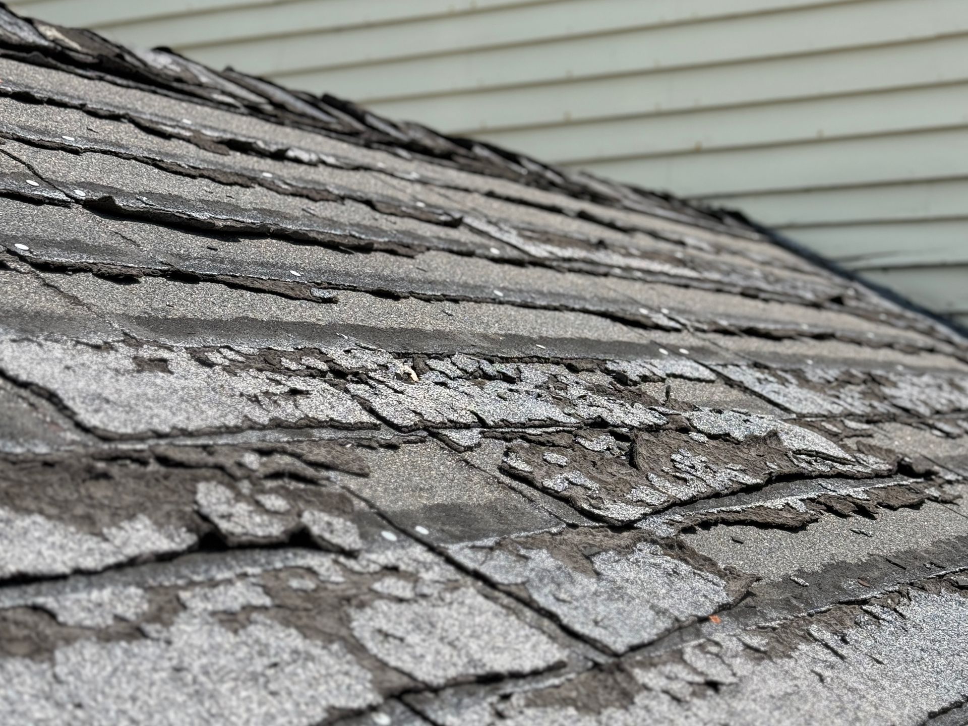 Extremely weathered asphalt roof shingles showing severe granule loss, cracking, and deterioration.