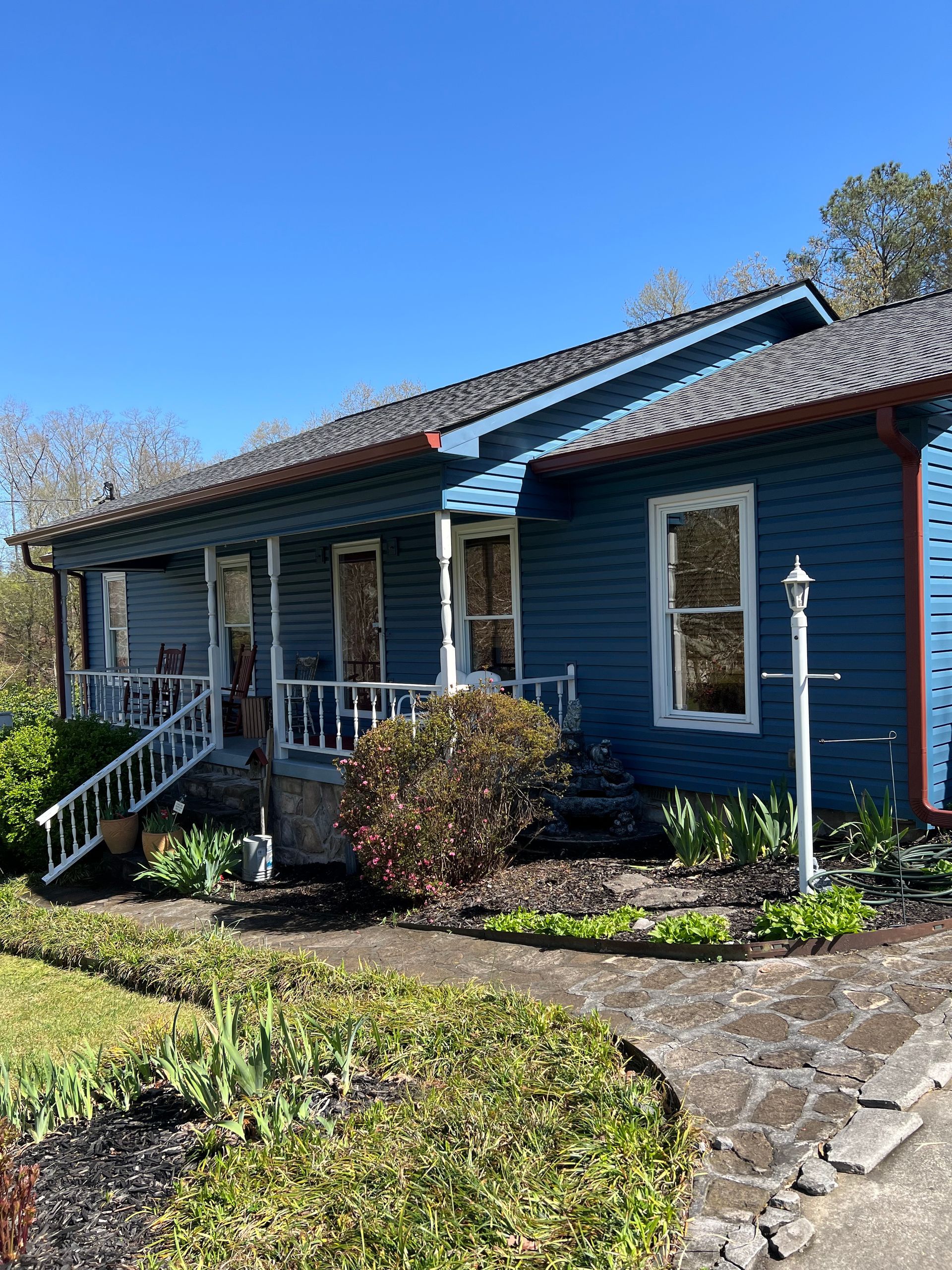 A blue, single-story house with a white front porch railing and a stone walkway on a sunny day.