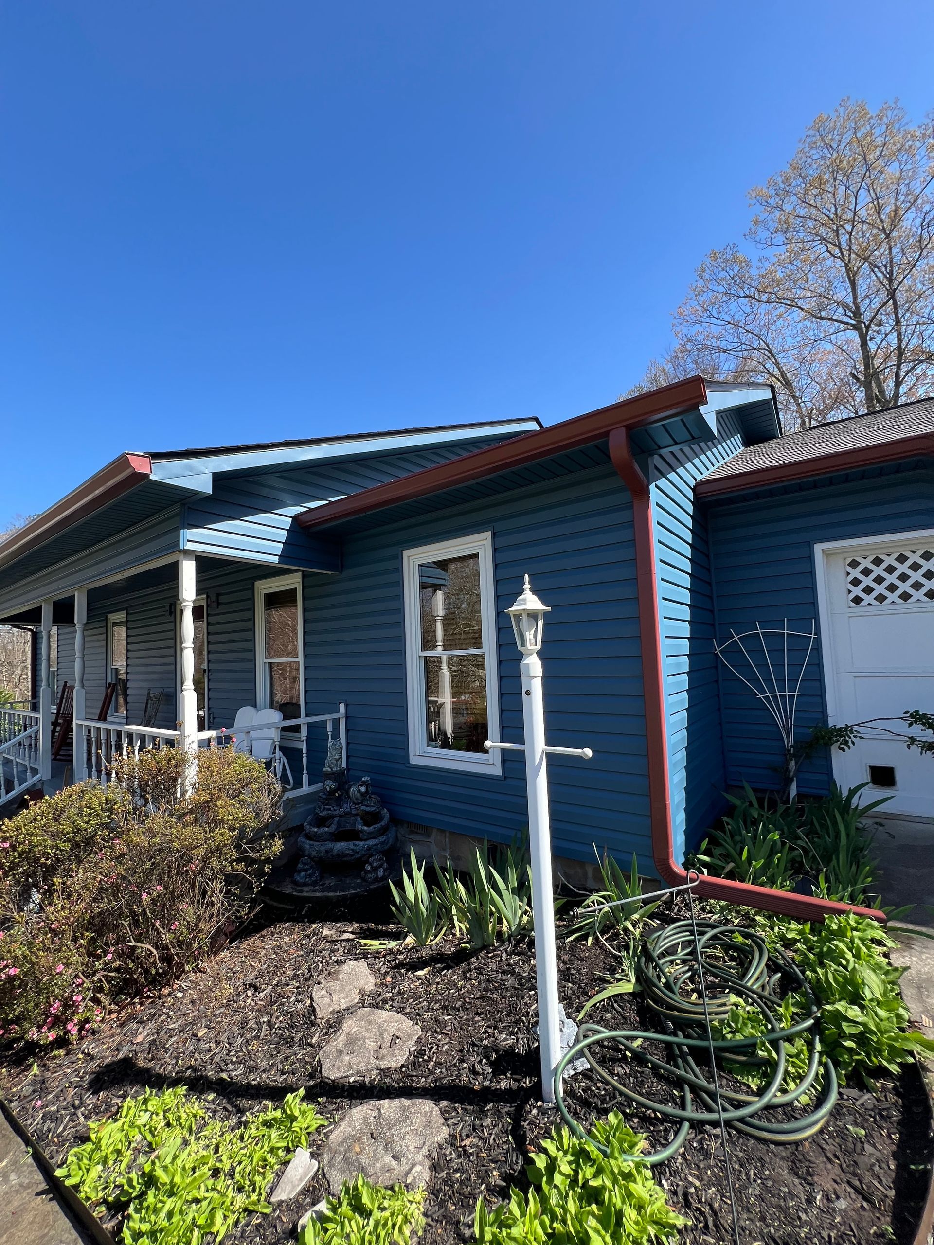 A single-story blue house with a covered front porch and a landscaped front garden on a bright, clear day.