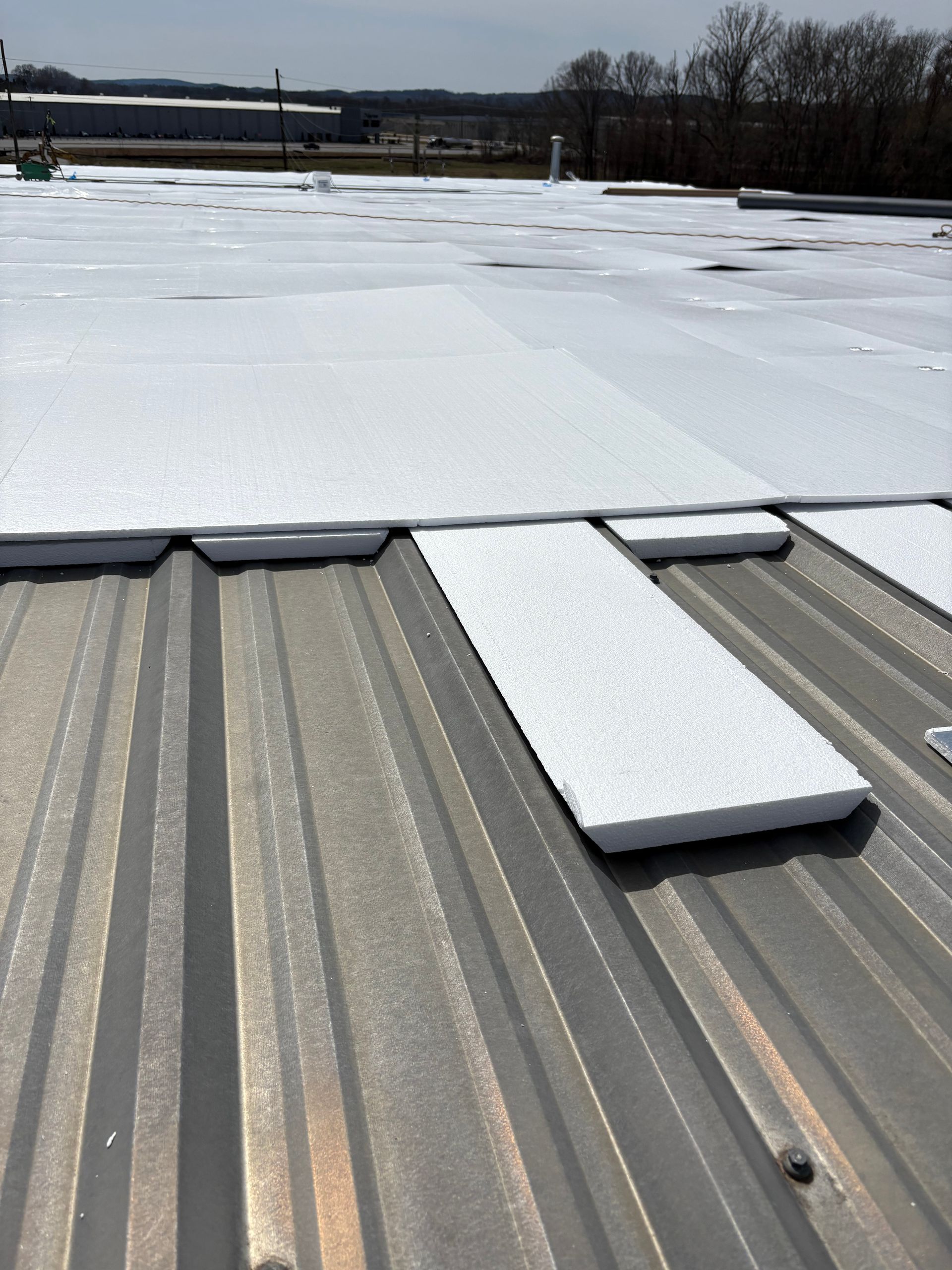 White insulation boards being installed over corrugated metal roofing on a sunny day.