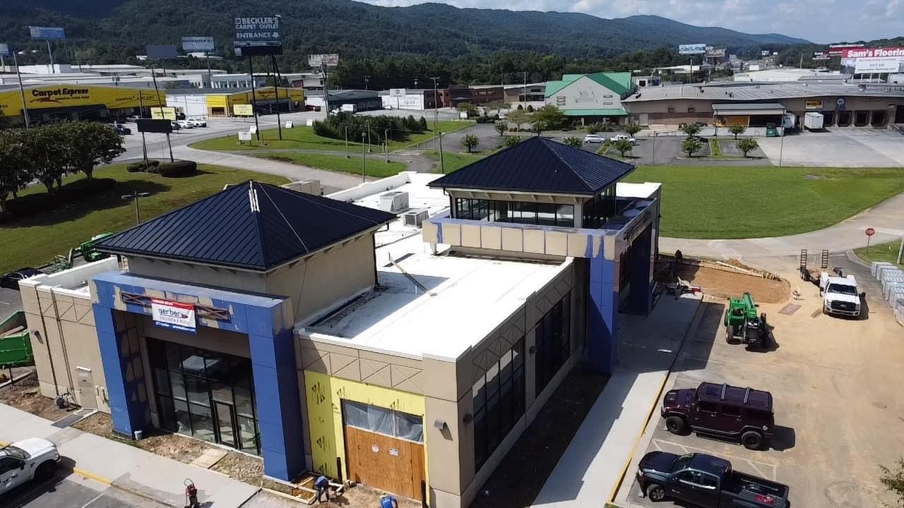 Aerial view of a commercial building under construction with blue trim, metal roofs, and surrounding parking lots.