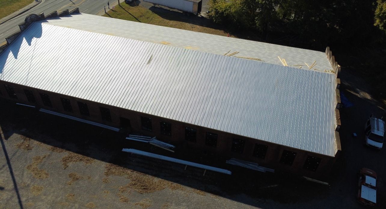 An aerial view of a long, rectangular building with a newly installed, reflective metal roof.