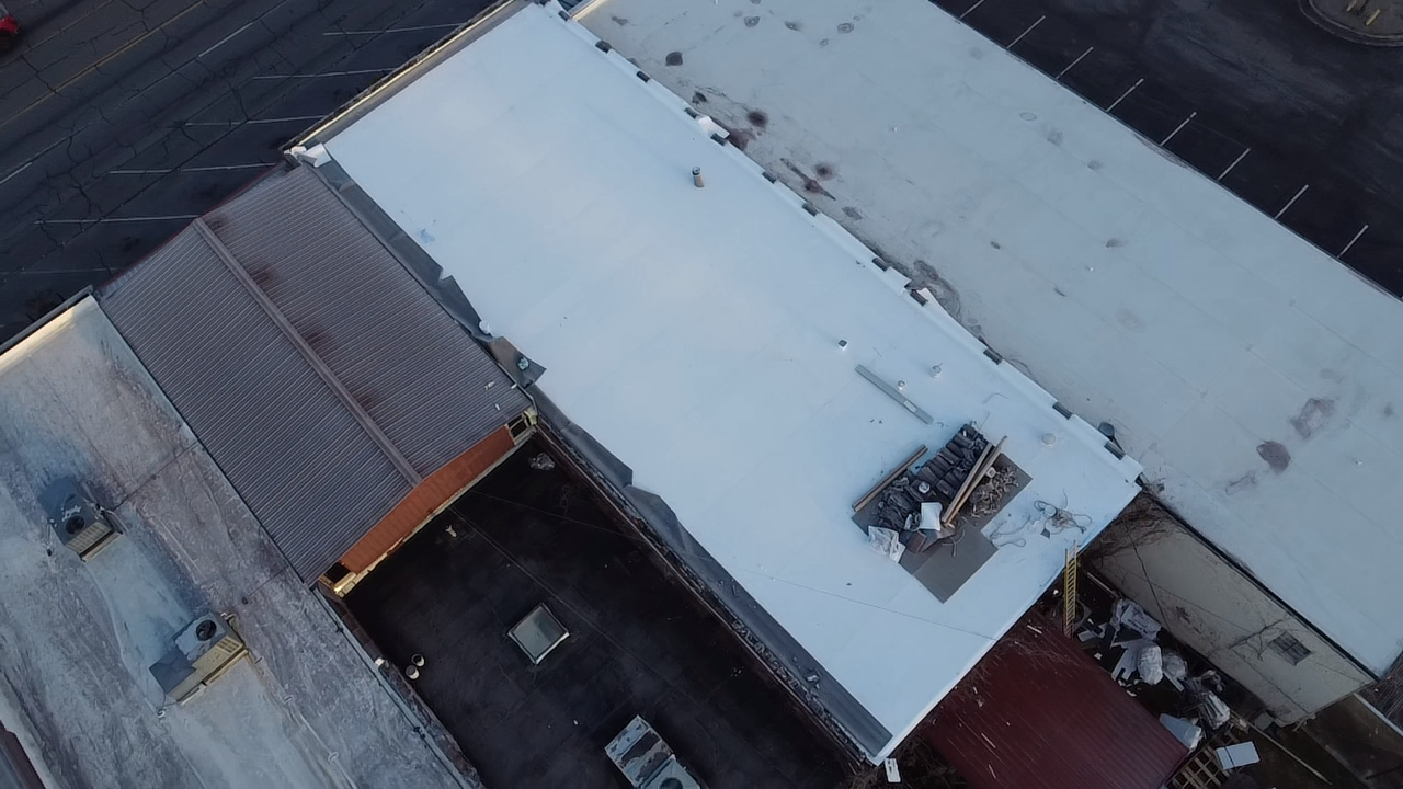 Aerial view of a flat, light-colored roof with HVAC units on a building adjacent to a smaller structure with a metal roof.