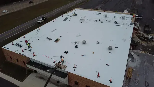 Aerial view of workers installing a white membrane roof on a brick commercial building near a road.