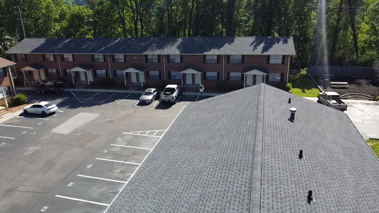An aerial view of a two-story brick apartment building and a parking lot with several parked cars.
