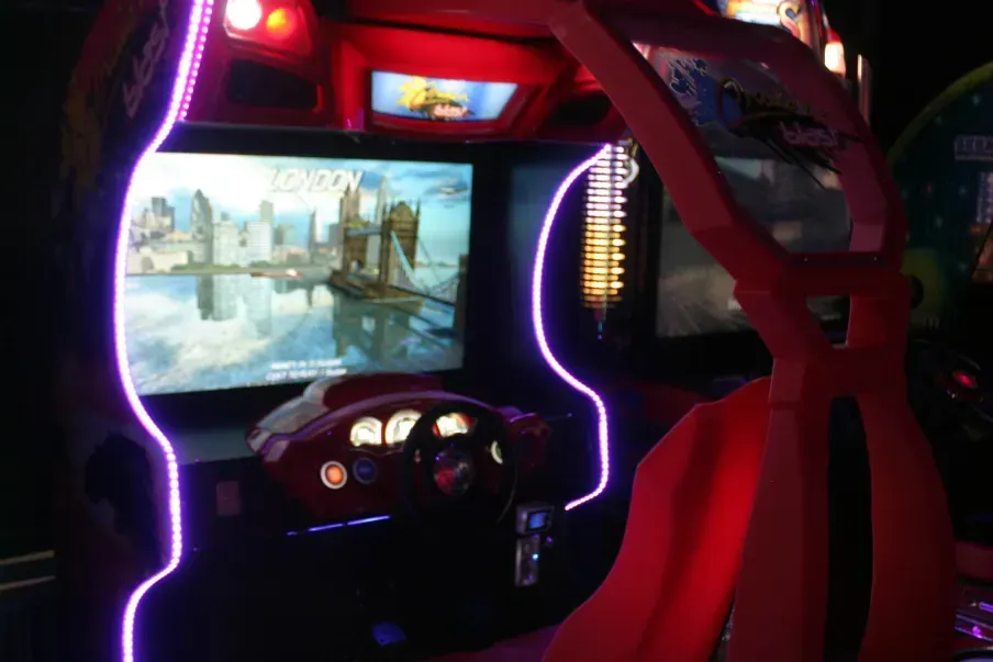 Arcade racing game, red and black, with steering wheel and large screen displaying a city scene.
