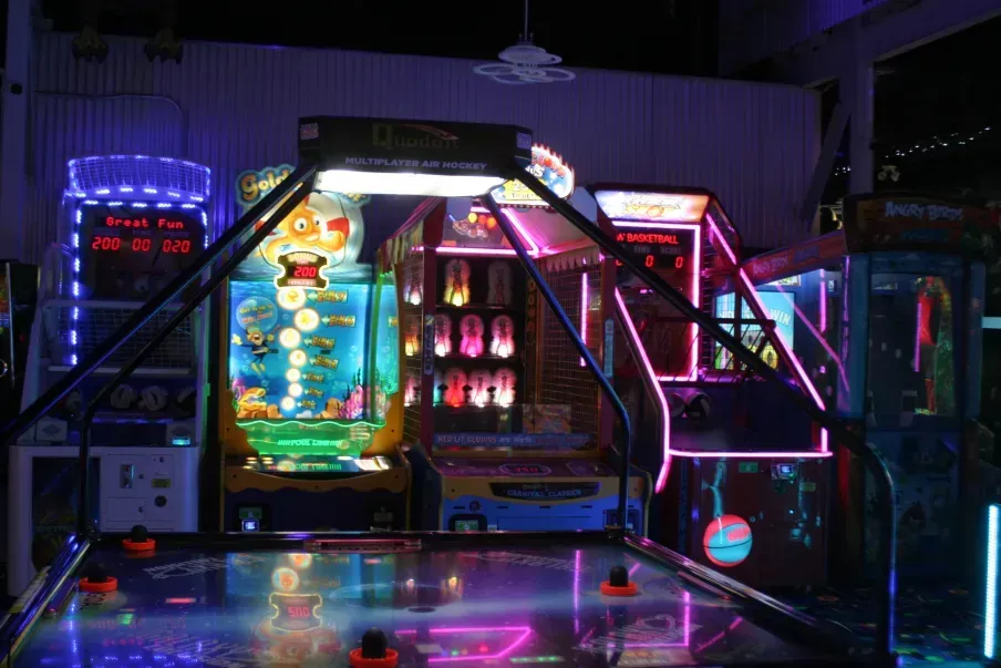 Arcade with colorful, illuminated game machines; air hockey table in foreground.
