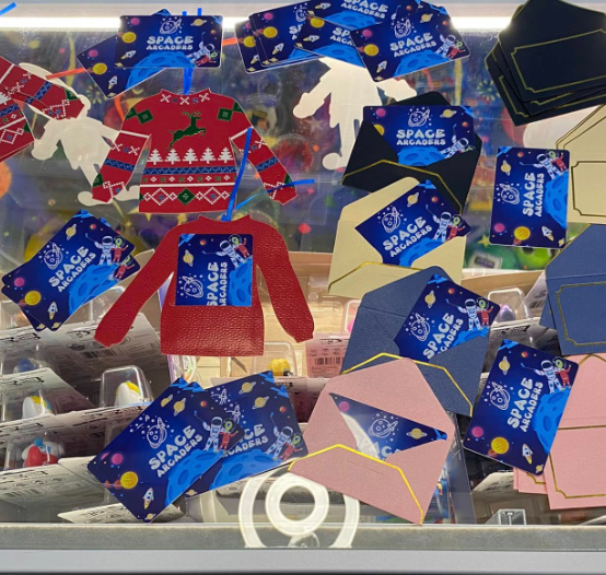 Holiday sweater-shaped tags and Space Arcaders cards in various colored envelopes, on a display.