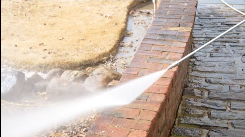 A person is using a high pressure washer to clean a brick wall.