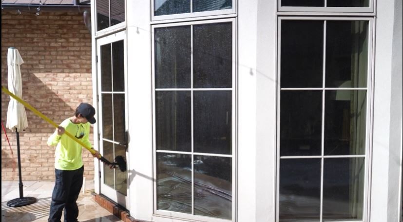 A man is cleaning the windows of a house with a broom.