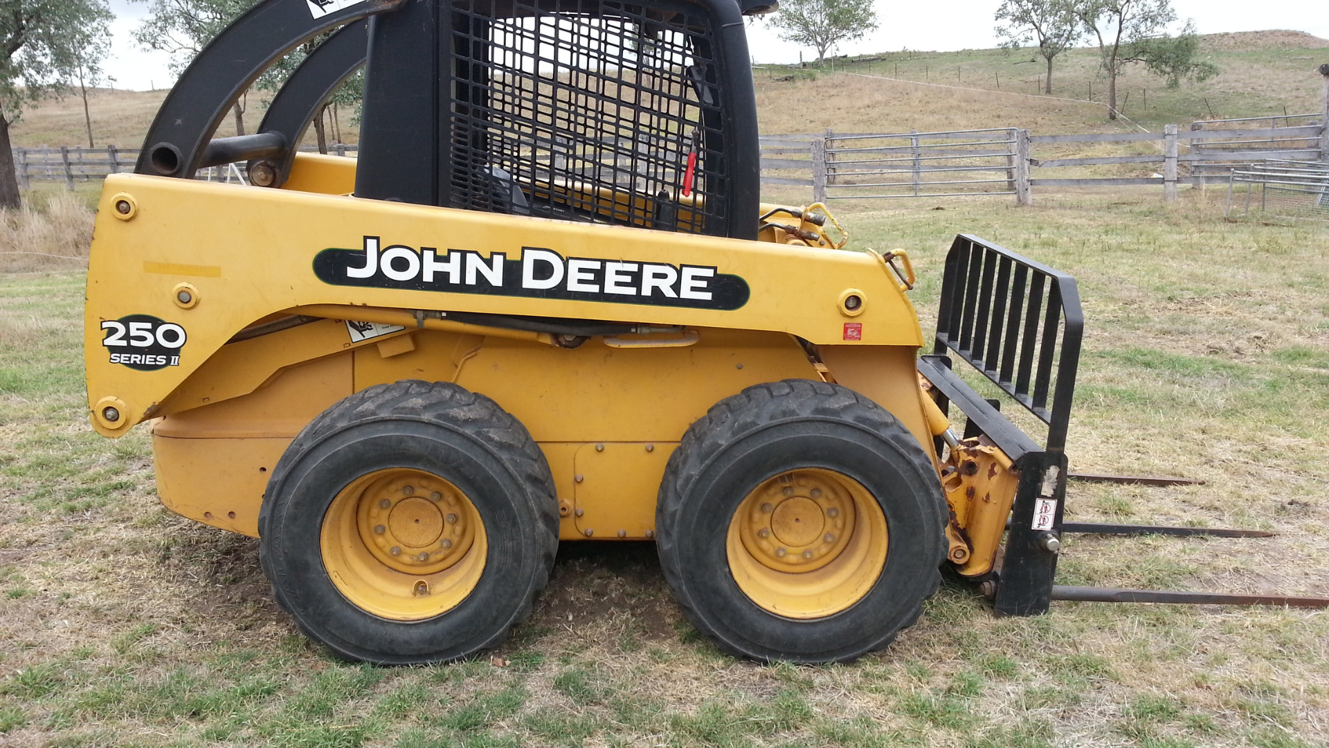 A yellow john deere skid steer is parked in a grassy field