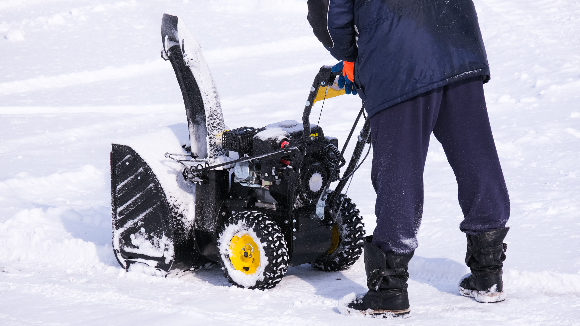 A man is standing next to a snow blower in the snow.