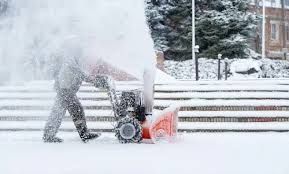 Person clearing heavy snow with a snowblower on a snowy walkway outdoors