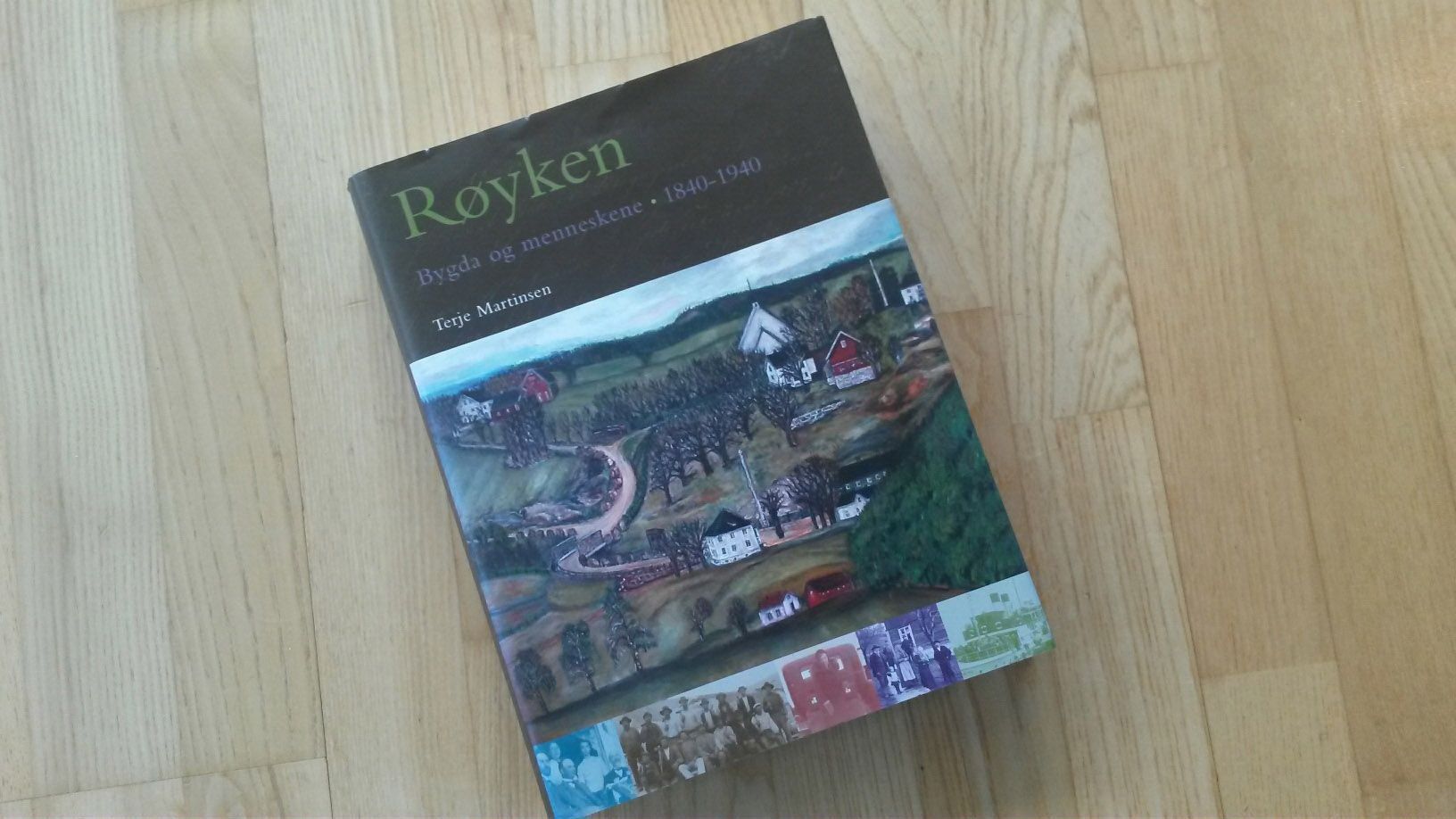 Bok med tittelen «Røyken» med landskapsillustrasjon på tregulv.