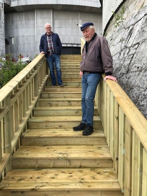 To menn står på nybygde utendørs trapper i tre.