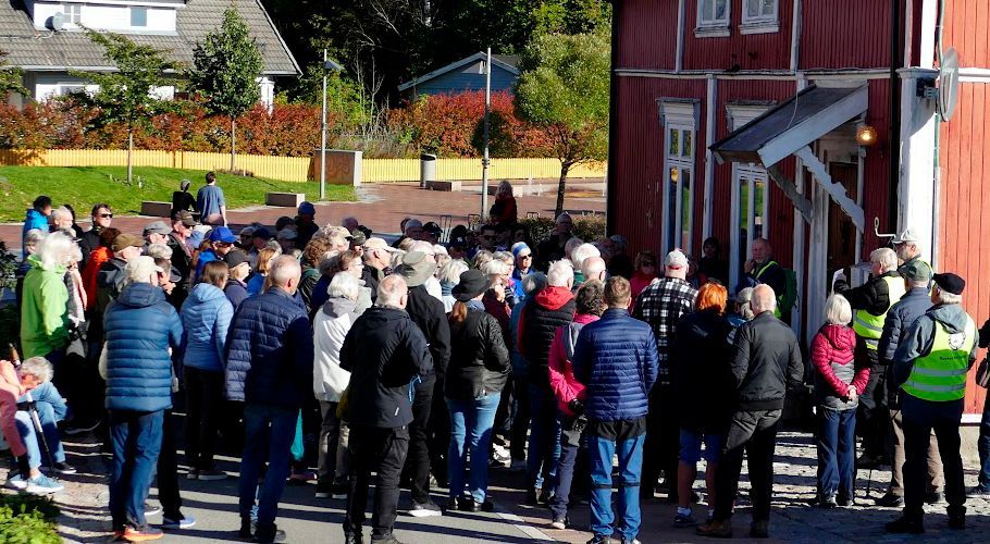 Stor folkemengde samlet seg utenfor en rød bygning på en solskinnsdag. Folk har på seg jakker, og noen har refleksvester.