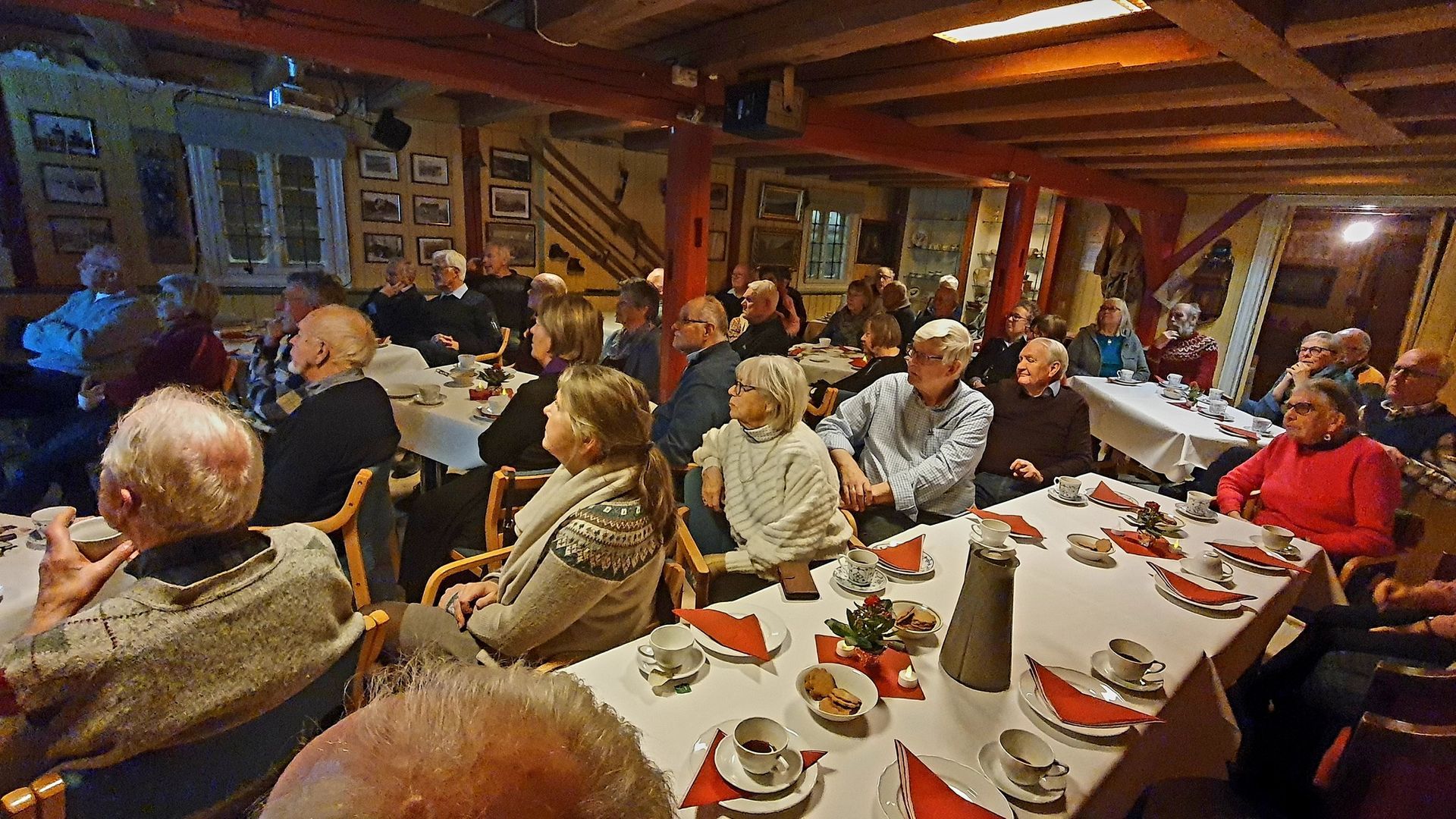 Kvinne spinner ull, barn ser på. Inne, gammelt hus, garn utstilt.