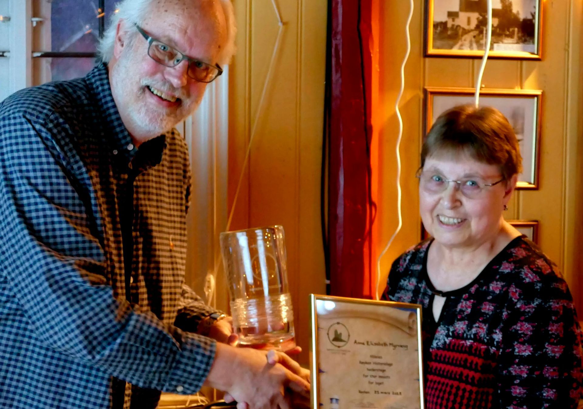Mann med briller, rutete skjorte, gir en glasskrukke til en kvinne som holder en prisplakett.