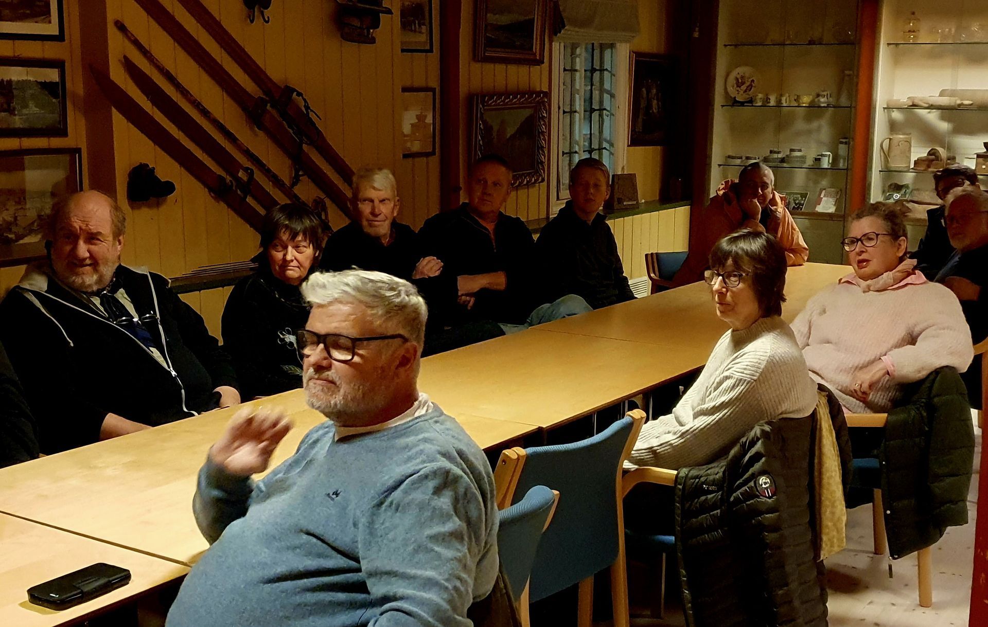 Gruppe mennesker sitter ved et langt bord i et rom med trepanel, og har et møte eller en diskusjon.