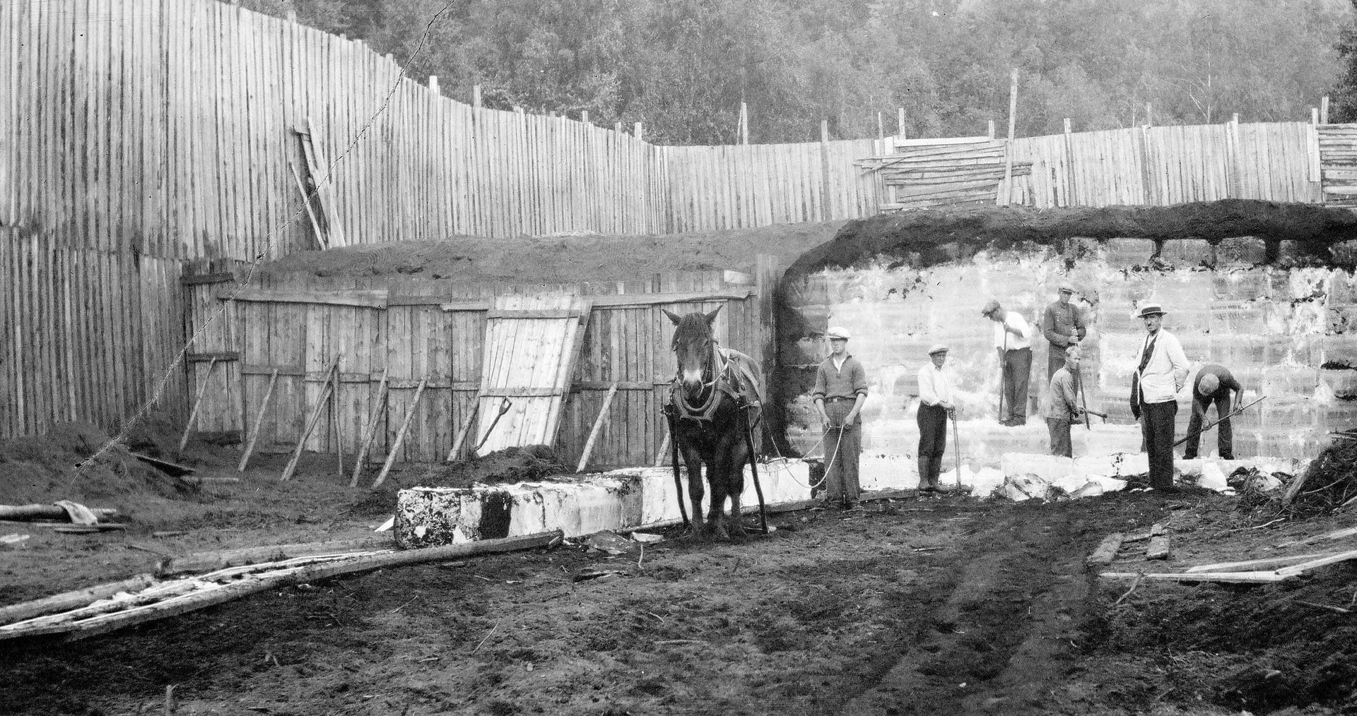 Byggeplass med arbeidere og hest, muligens sent på 1800-tallet. Trevegger og steinkonstruksjon.