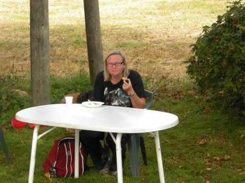 Person som sitter ved et hvitt bord, spiser ute, iført svarte klær og briller.