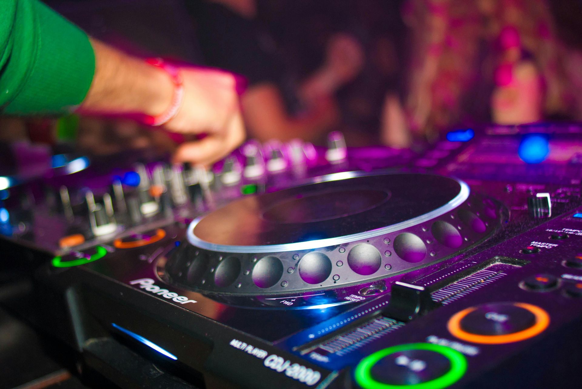 DJ at a club using a Pioneer CDJ-2000 nexus. Purple and blue lights, blurred background.