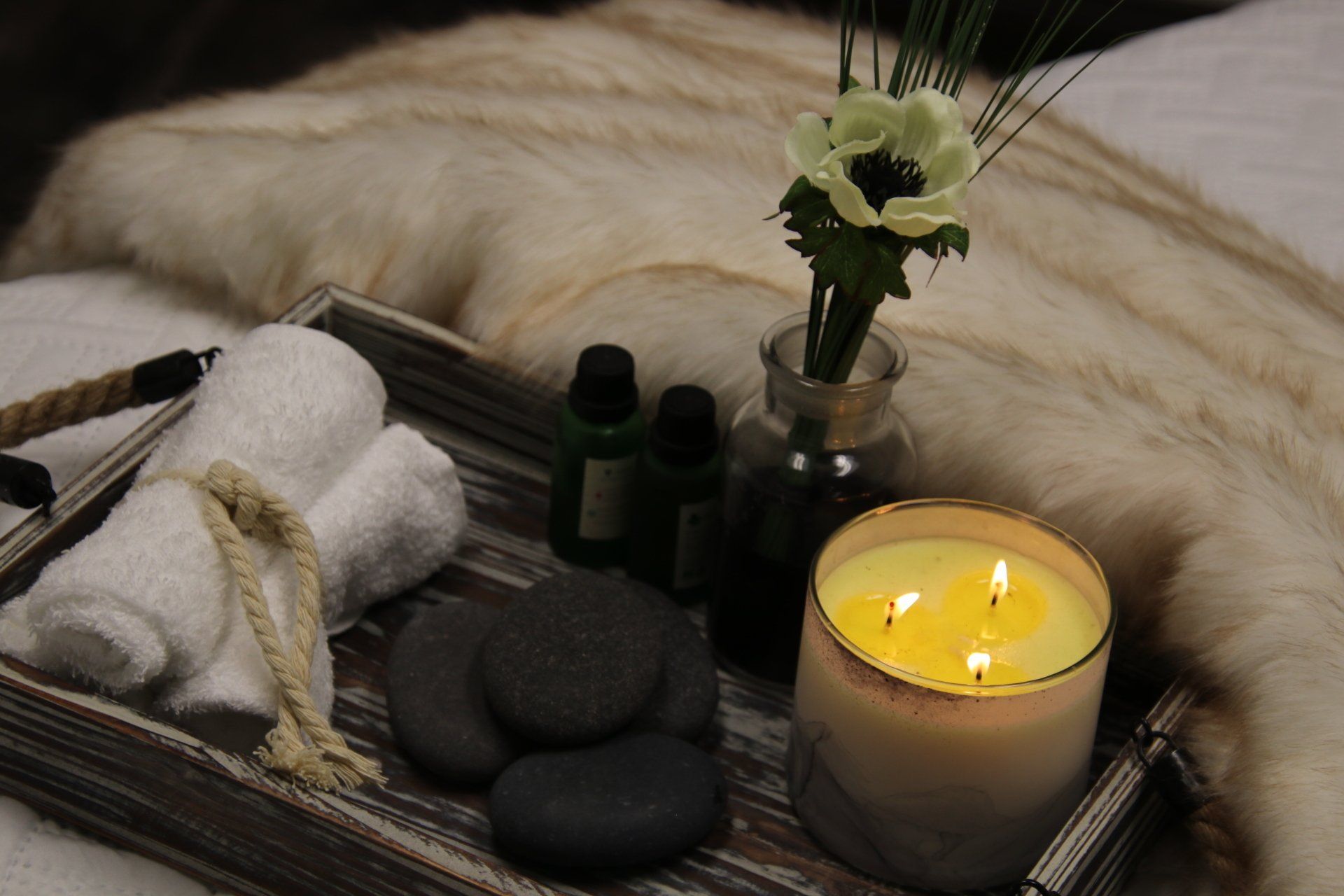 A wooden tray with a candle , rocks , towels and a vase of flowers at Results Skincare Studio in Fort Myers