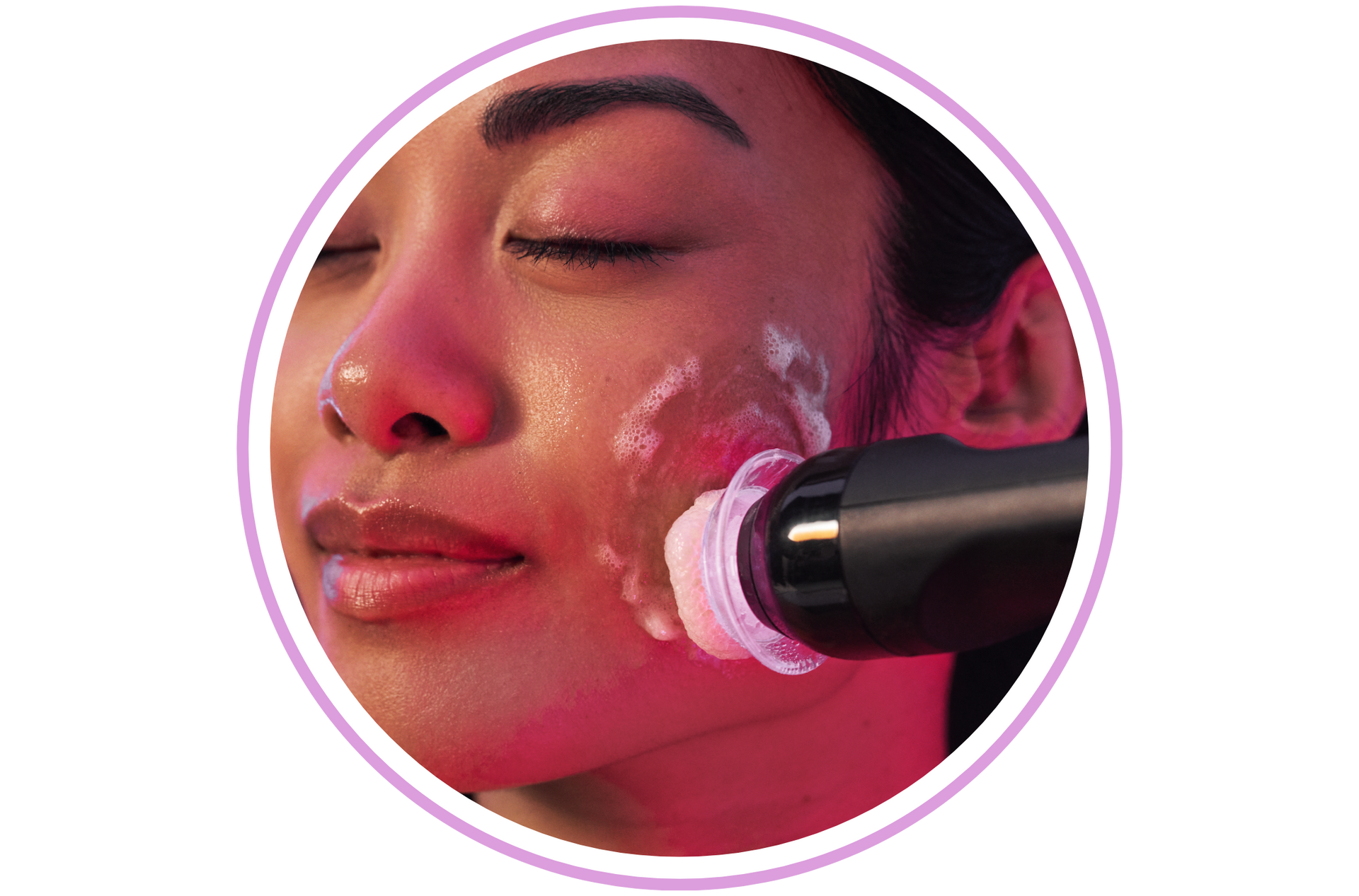 Woman receiving facial treatment with device on her cheek, surrounded by pink light.