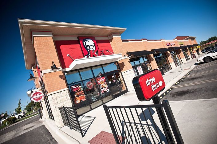 KFC restaurant with red sign, drive-thru, brick exterior, and blue sky.