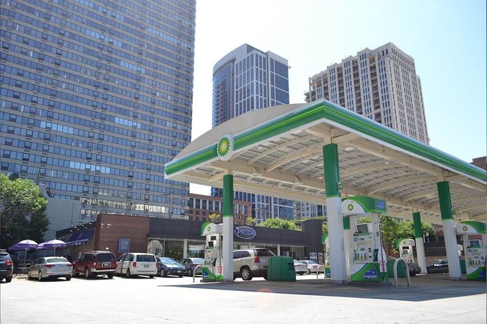 BP gas station in a city setting, with tall buildings in the background and cars parked nearby on a sunny day.