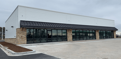 Exterior view of a commercial building with glass windows, a dark awning, and stone accents.