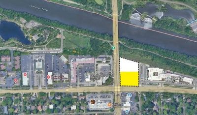 Aerial view of a city intersection with a yellow-highlighted vacant lot. River and buildings visible.