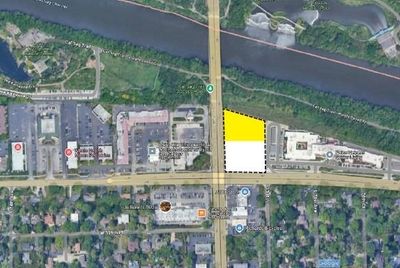Aerial view of a city area with a river, bridge, roads, buildings, and parking lots. A yellow highlighted area is on the right.