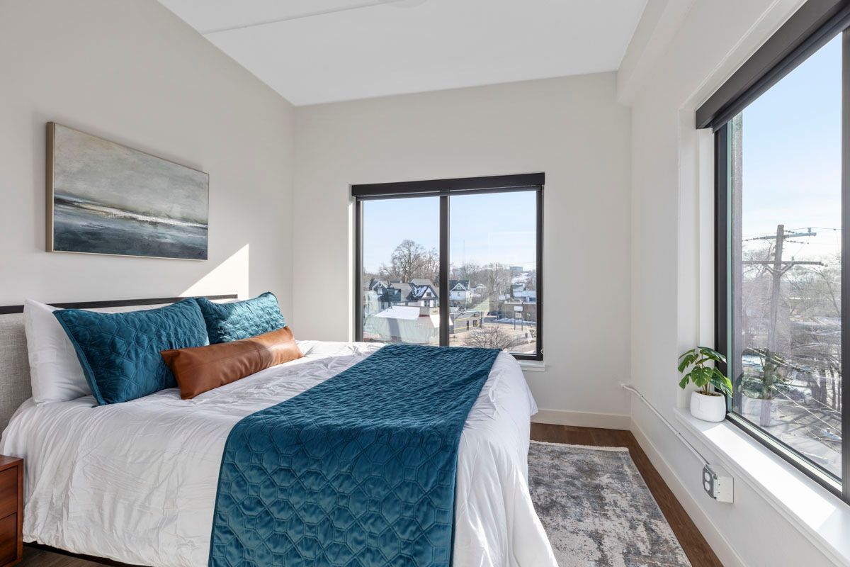 Bright bedroom with a bed, teal bedding, and large windows overlooking snowy trees